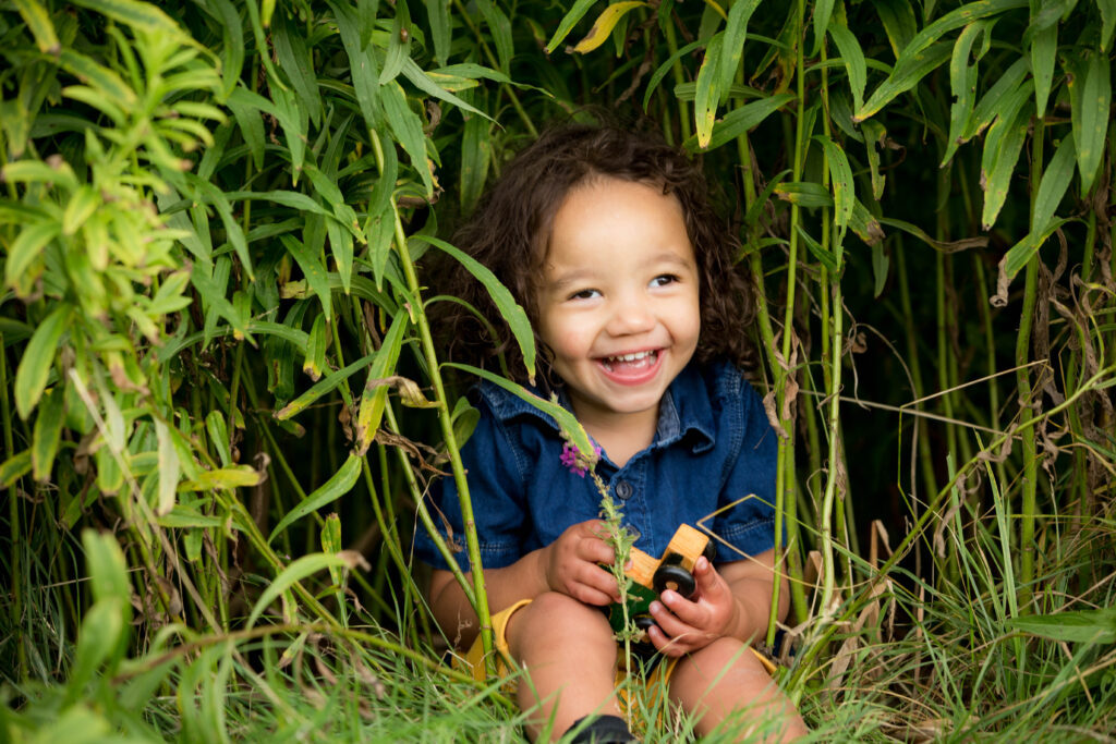 A kid sitting in bushes smiling.